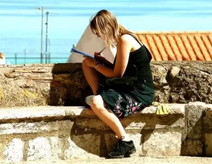 Una mujer escribe en un cuaderno sentada sobre una muralla